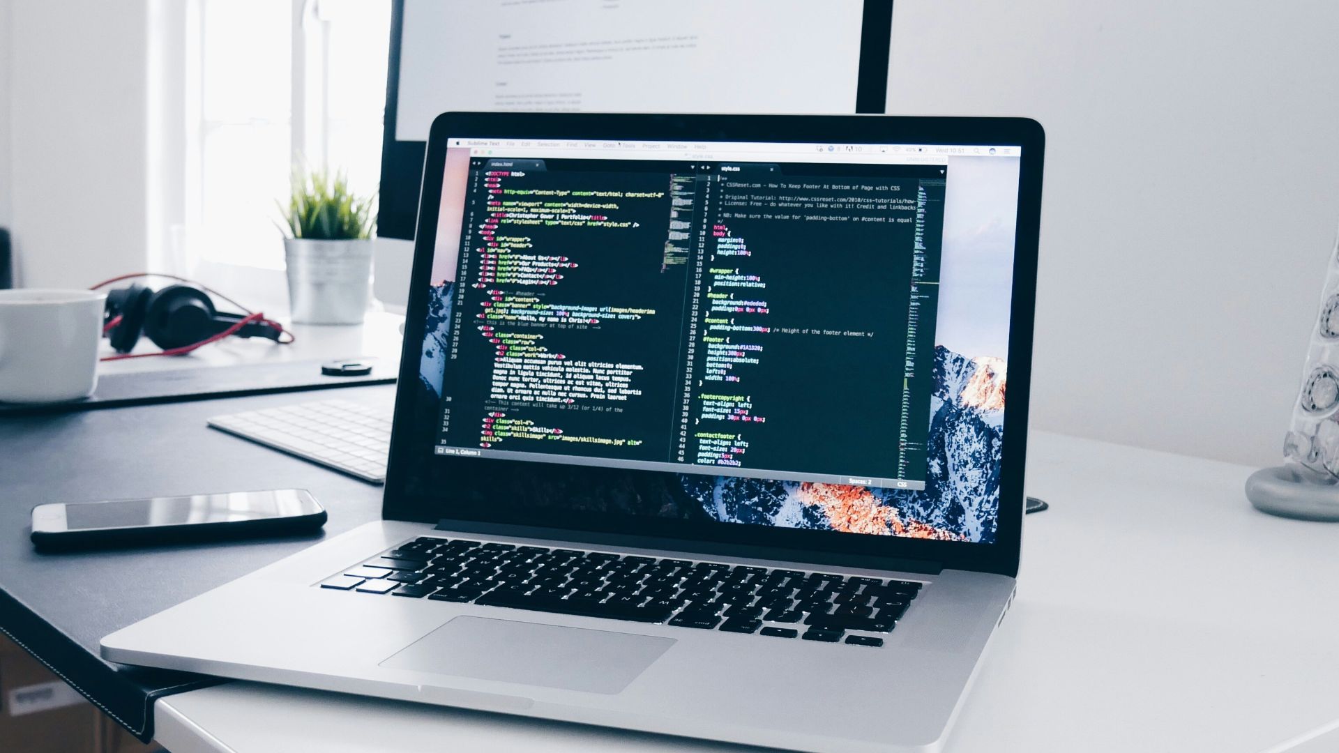 A MacBook with lines of code on its screen on a busy desk