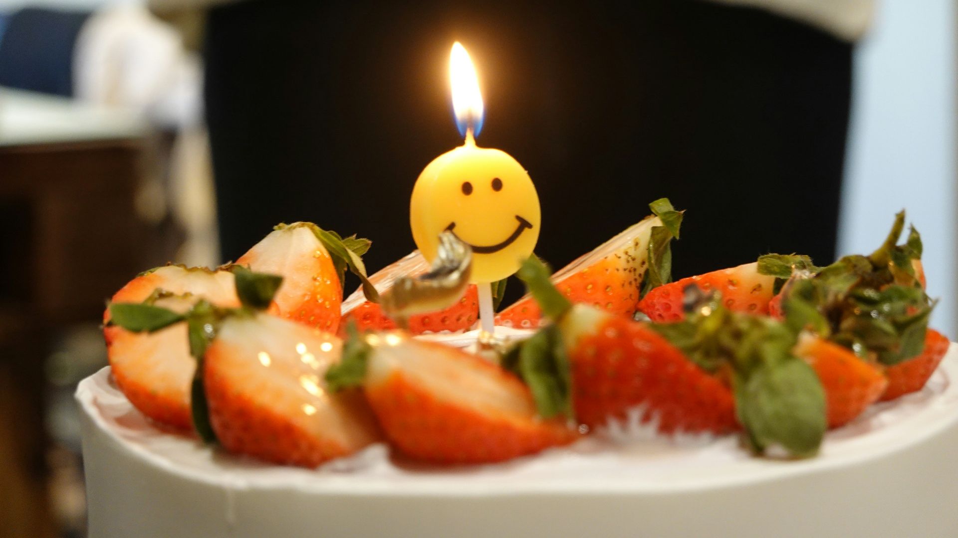 a birthday cake with strawberries and a smiley face candle