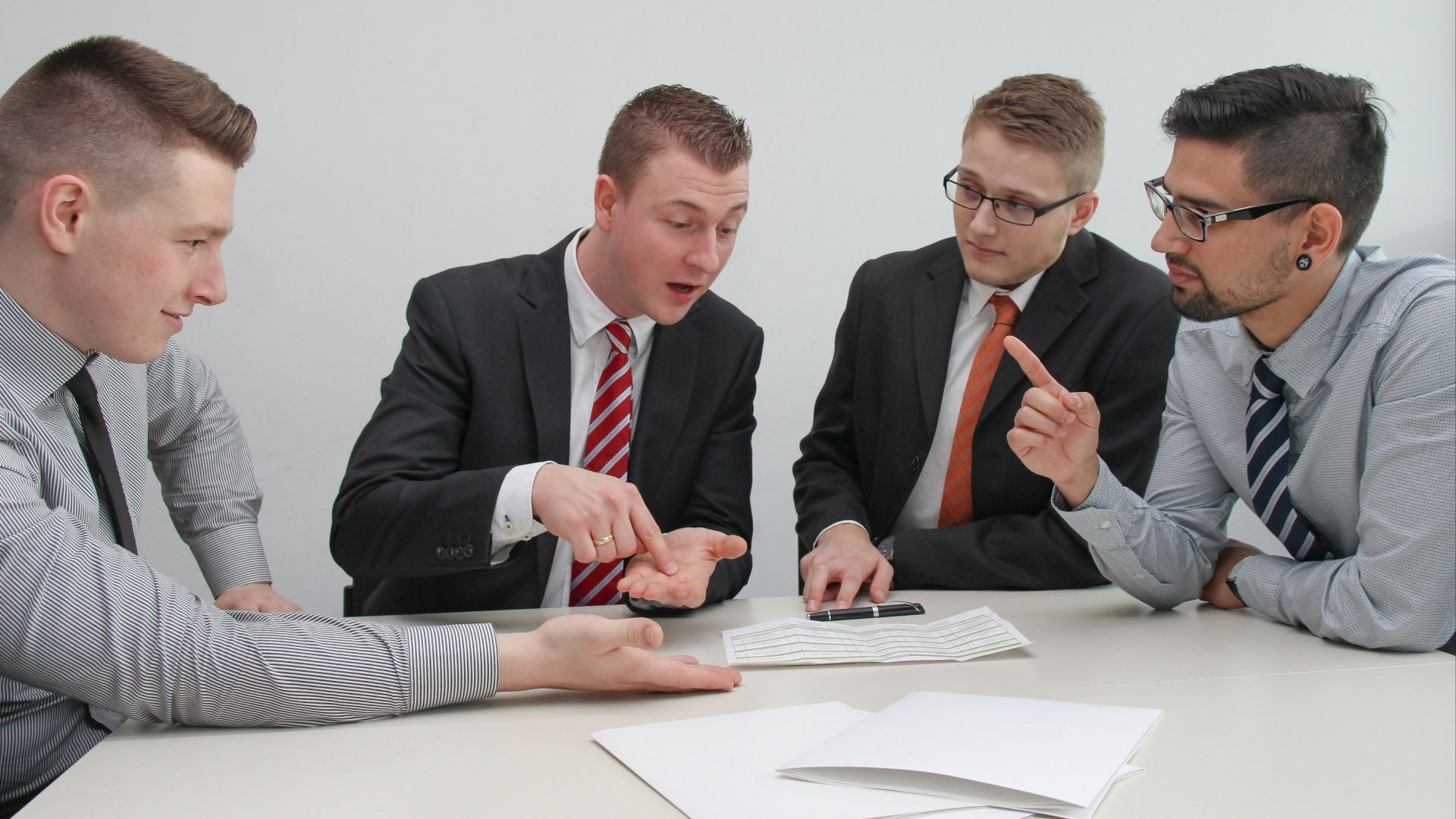 four men sitting at desk talking