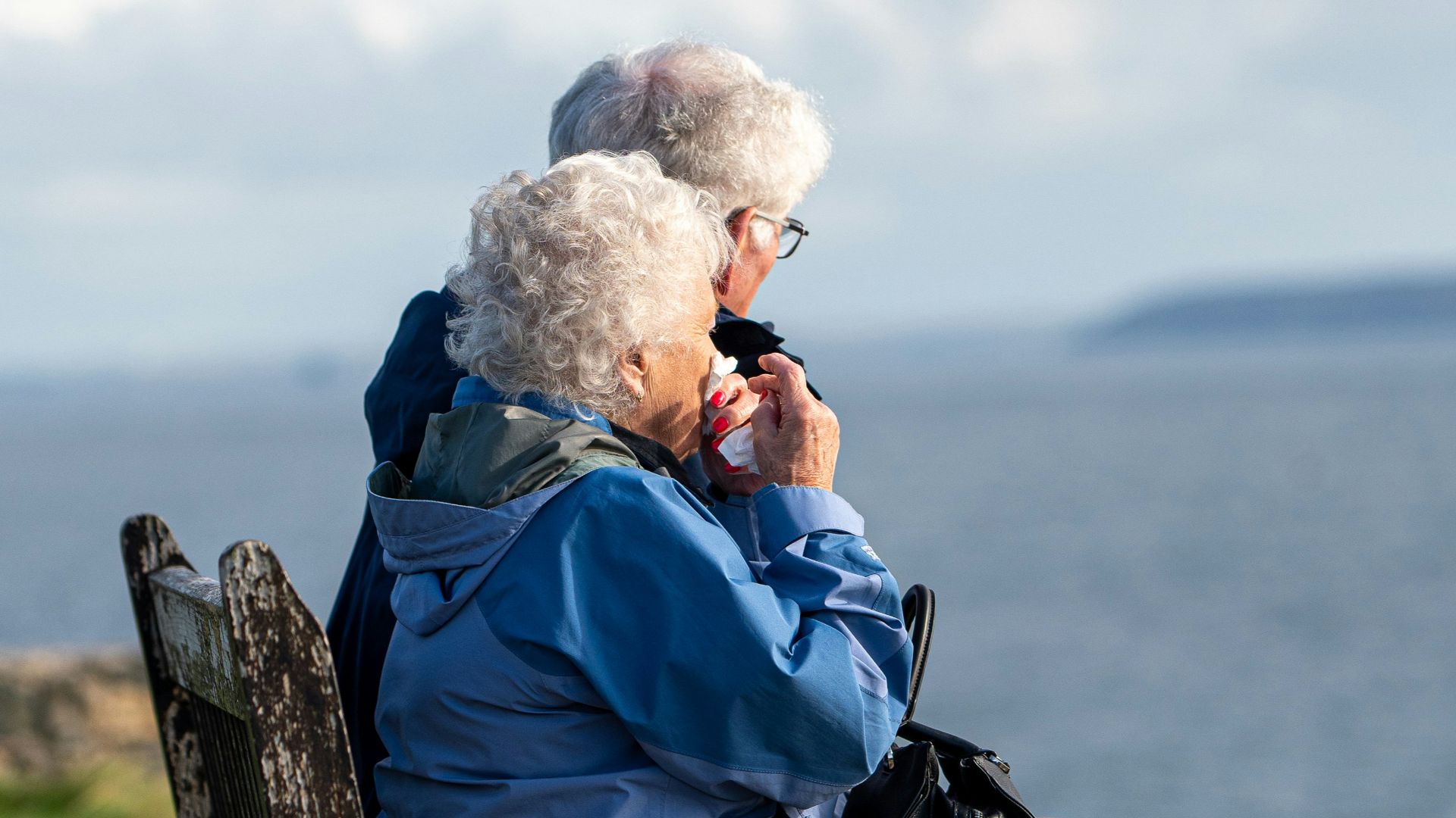 man and woman sitting on gray wooden bench viewing blue sea during daytime