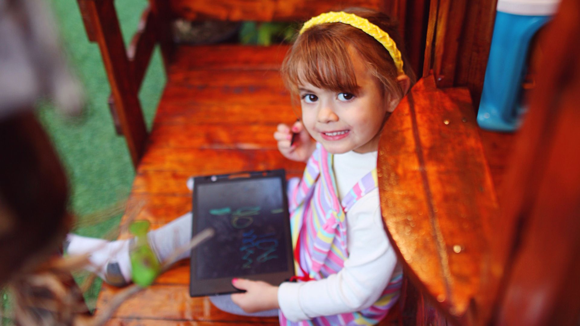 a little girl sitting on a wooden bench with a laptop