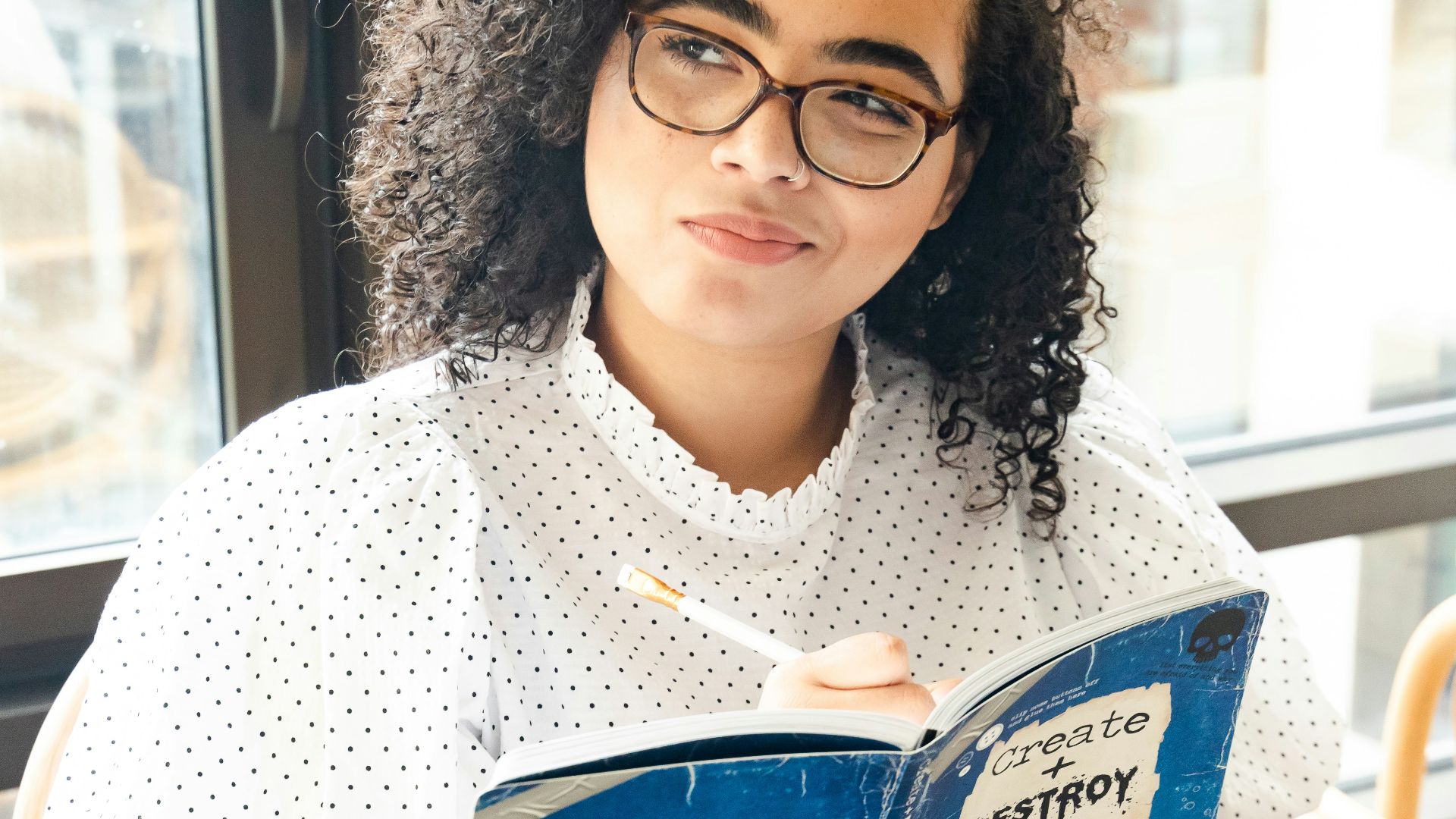 woman in white and black polka dot shirt holding blue and white book