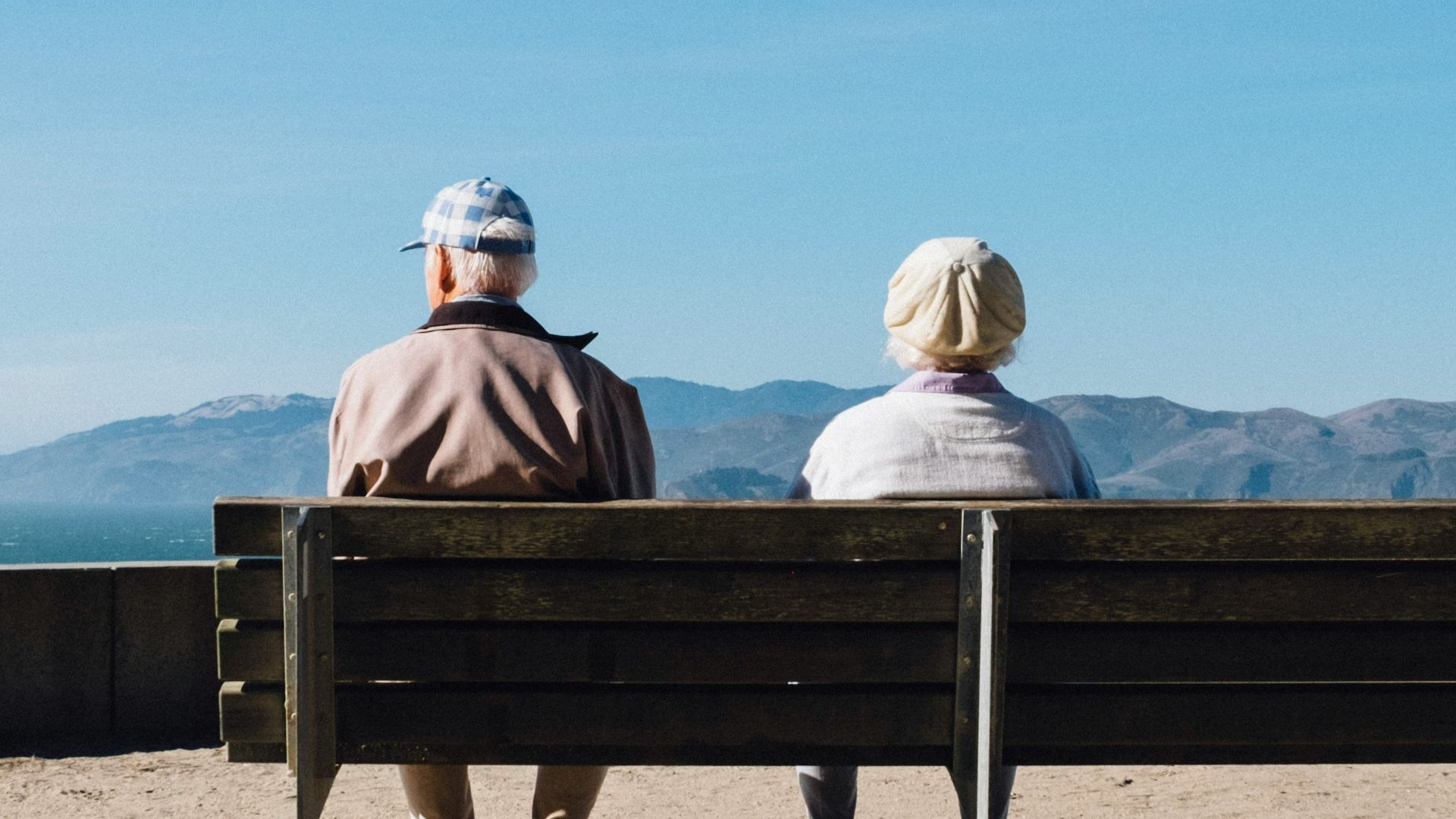 man and woman sitting on bench facing sea