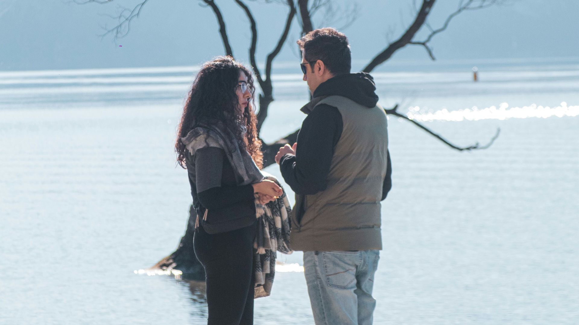 A man and woman standing on a beach next to a tree