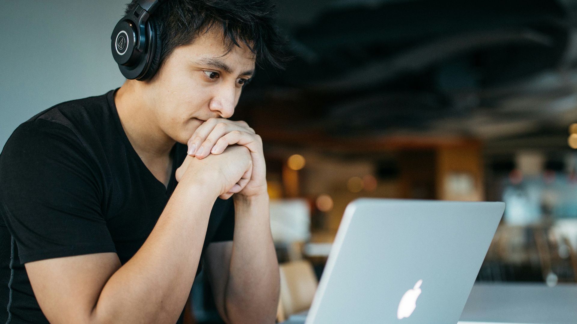 man wearing headphones while sitting on chair in front of MacBook