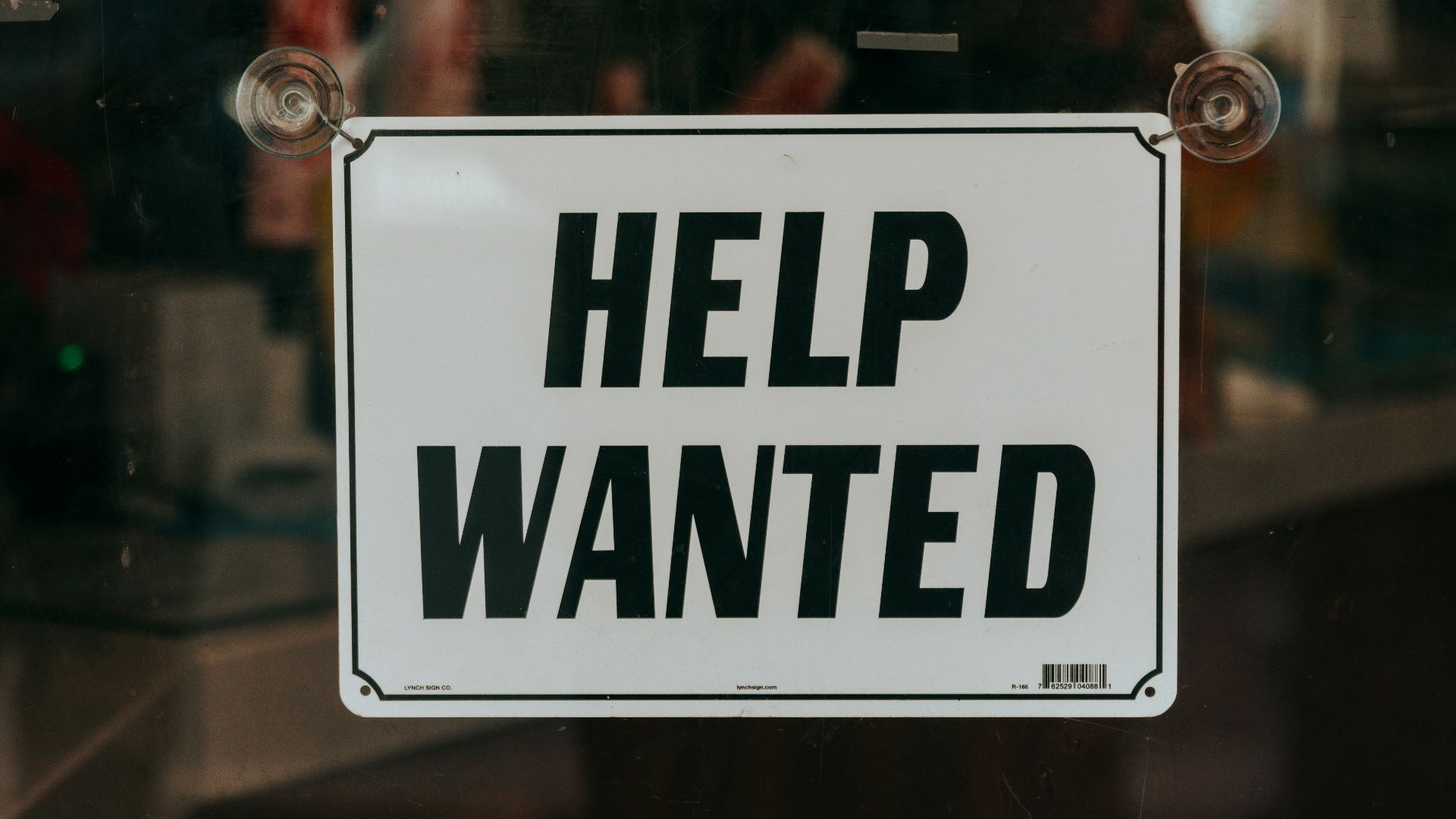 a sign that says help wanted in front of a window