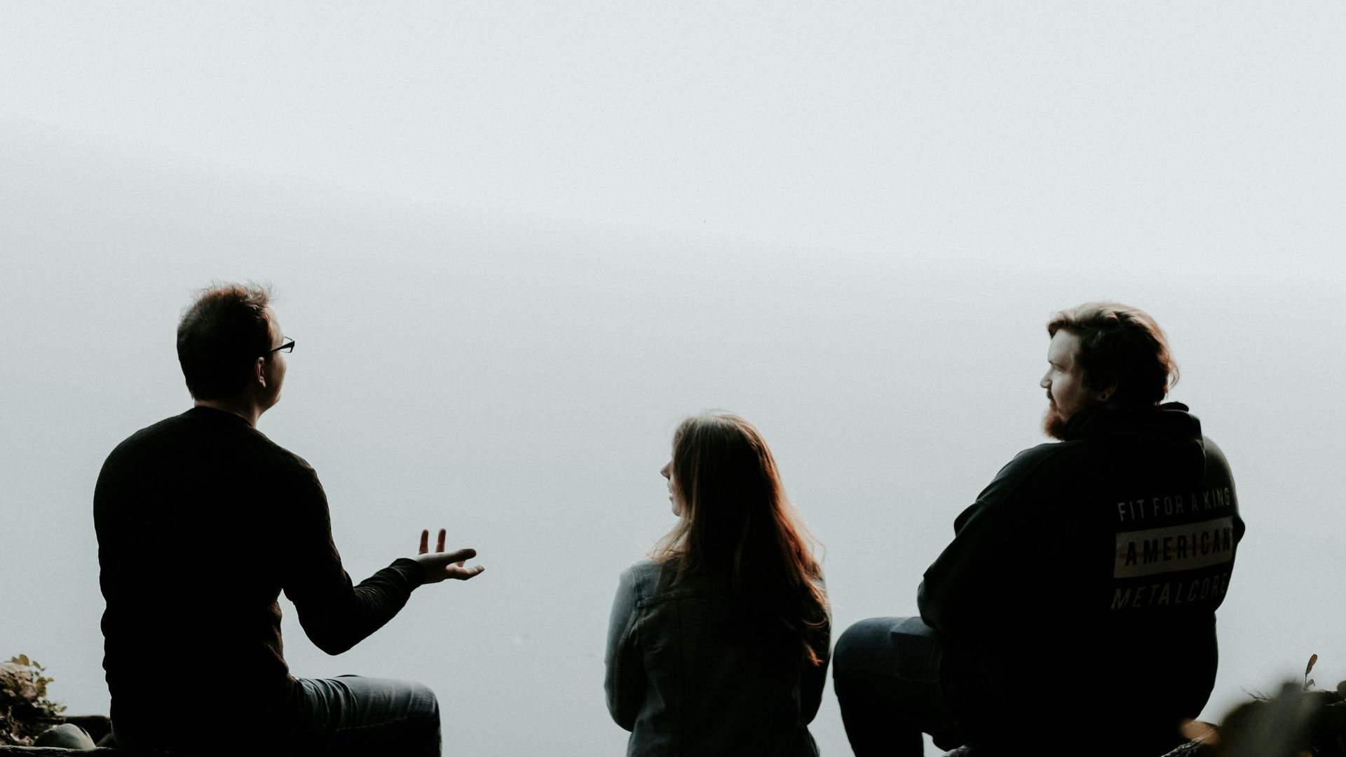silhouette of three people sitting on cliff under foggy weather