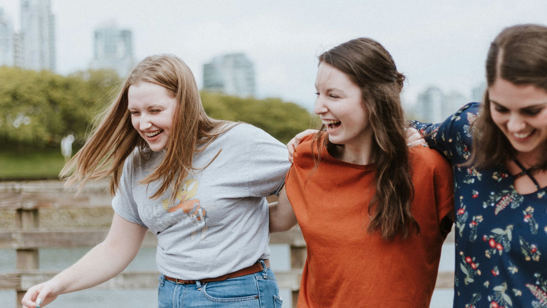 three women walking on brown wooden dock near high rise building during daytime