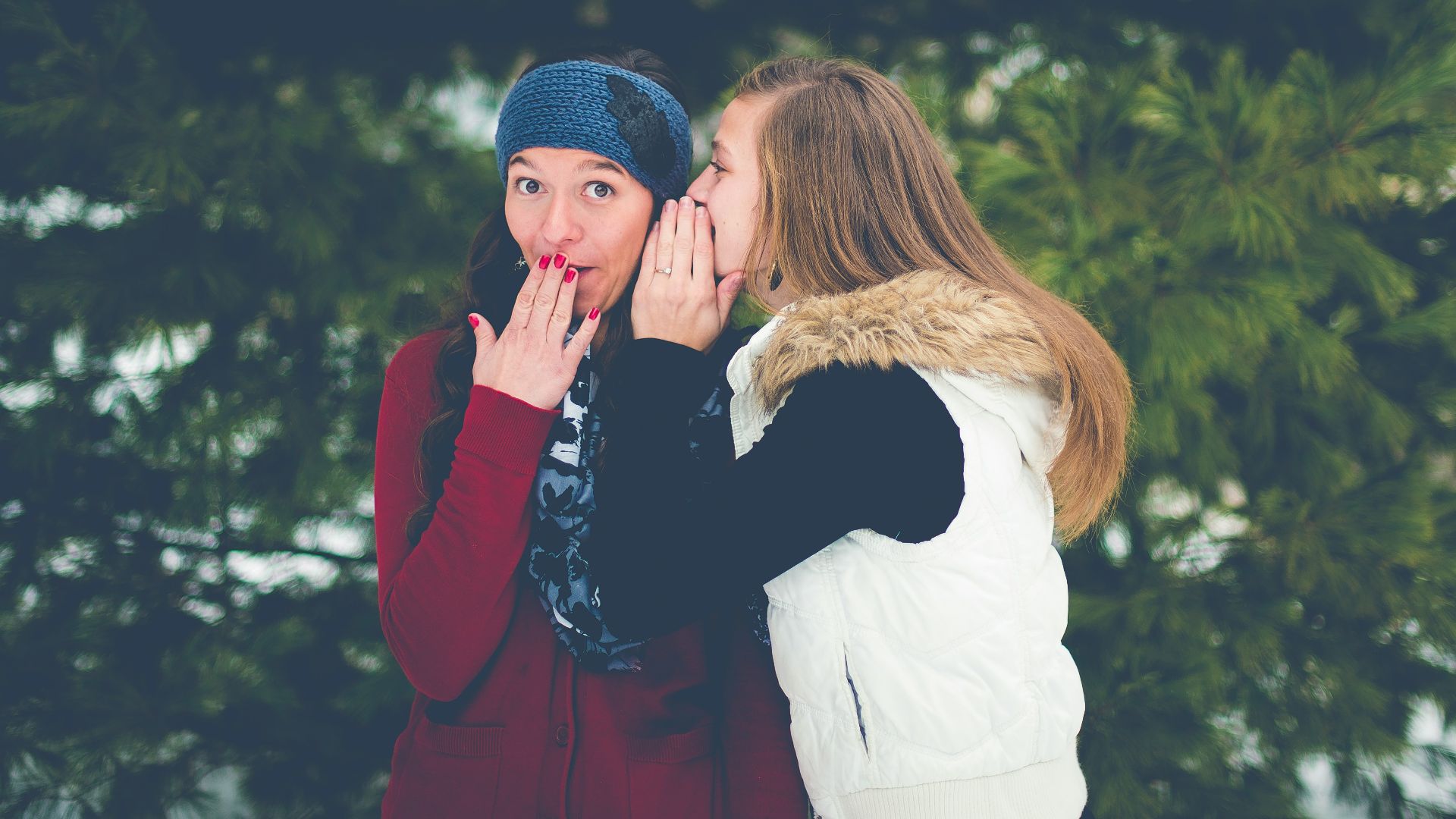 woman whispering on woman's ear while hands on lips