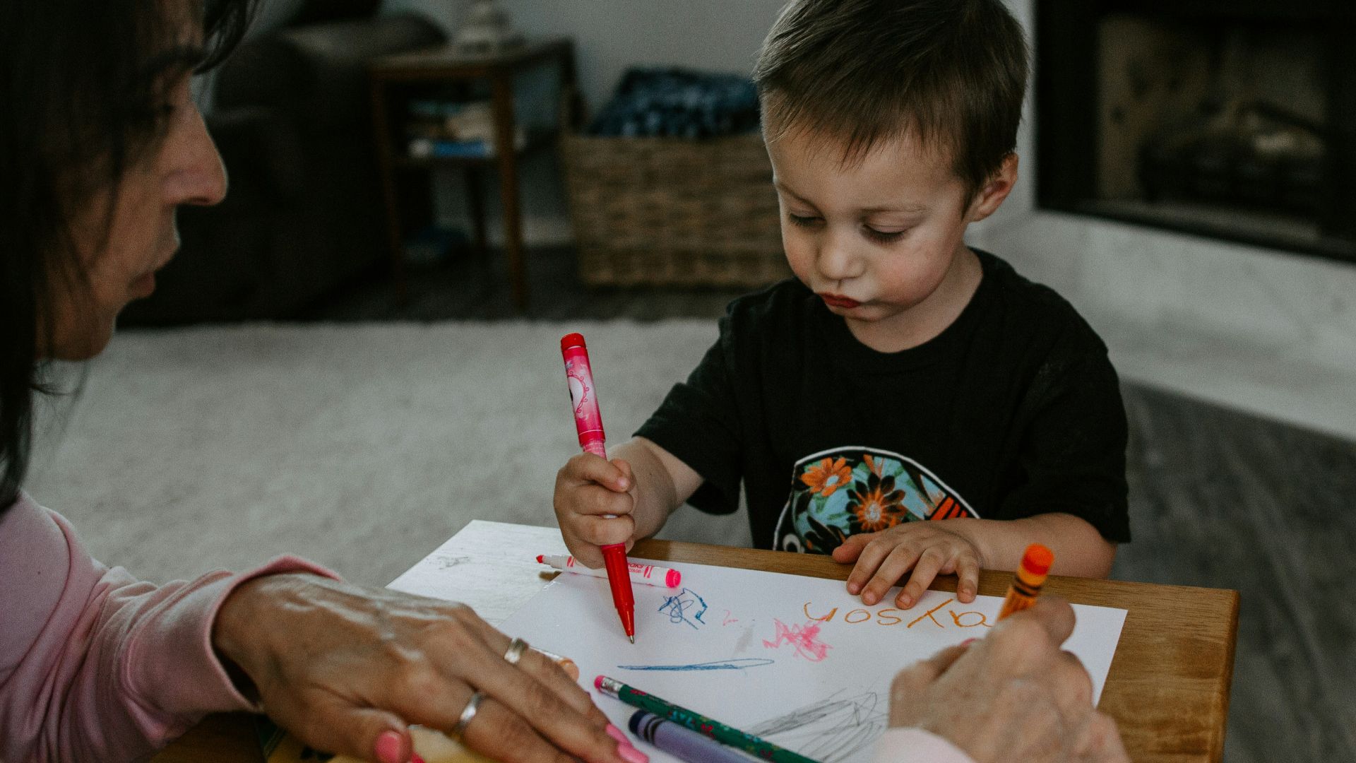 boy in black crew neck t-shirt holding pink pen writing on white paper