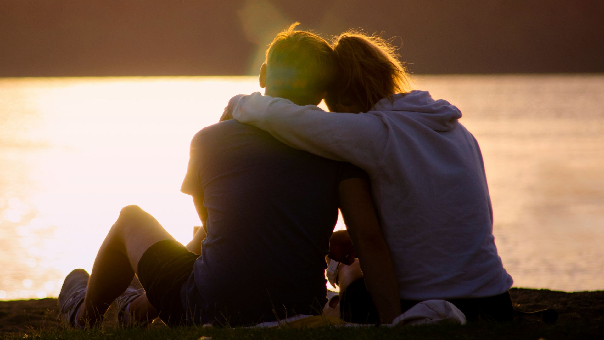 woman in black jacket sitting on green grass field near body of water during daytime