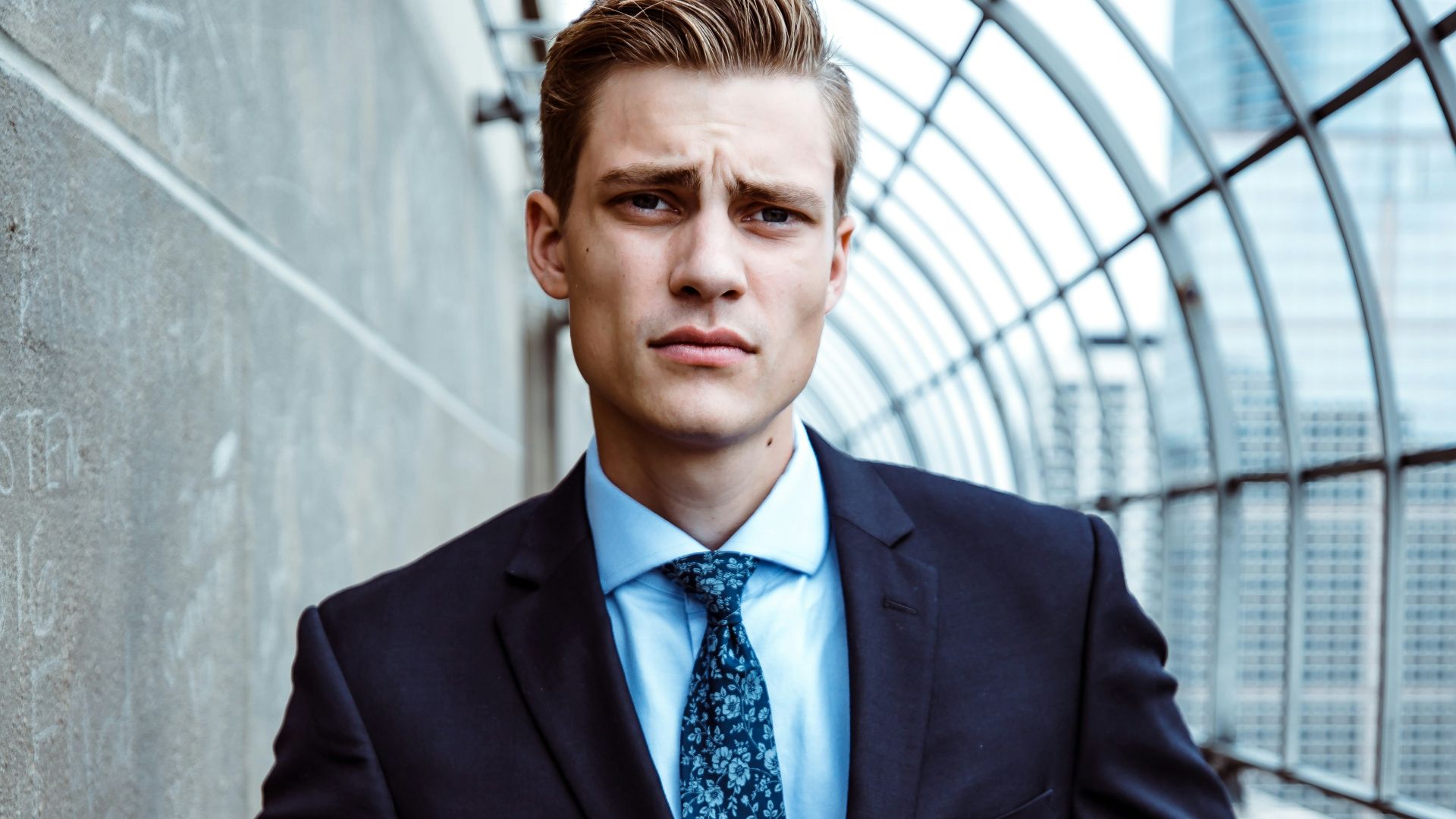 man wearing black and teal dress suit standing near gray wall