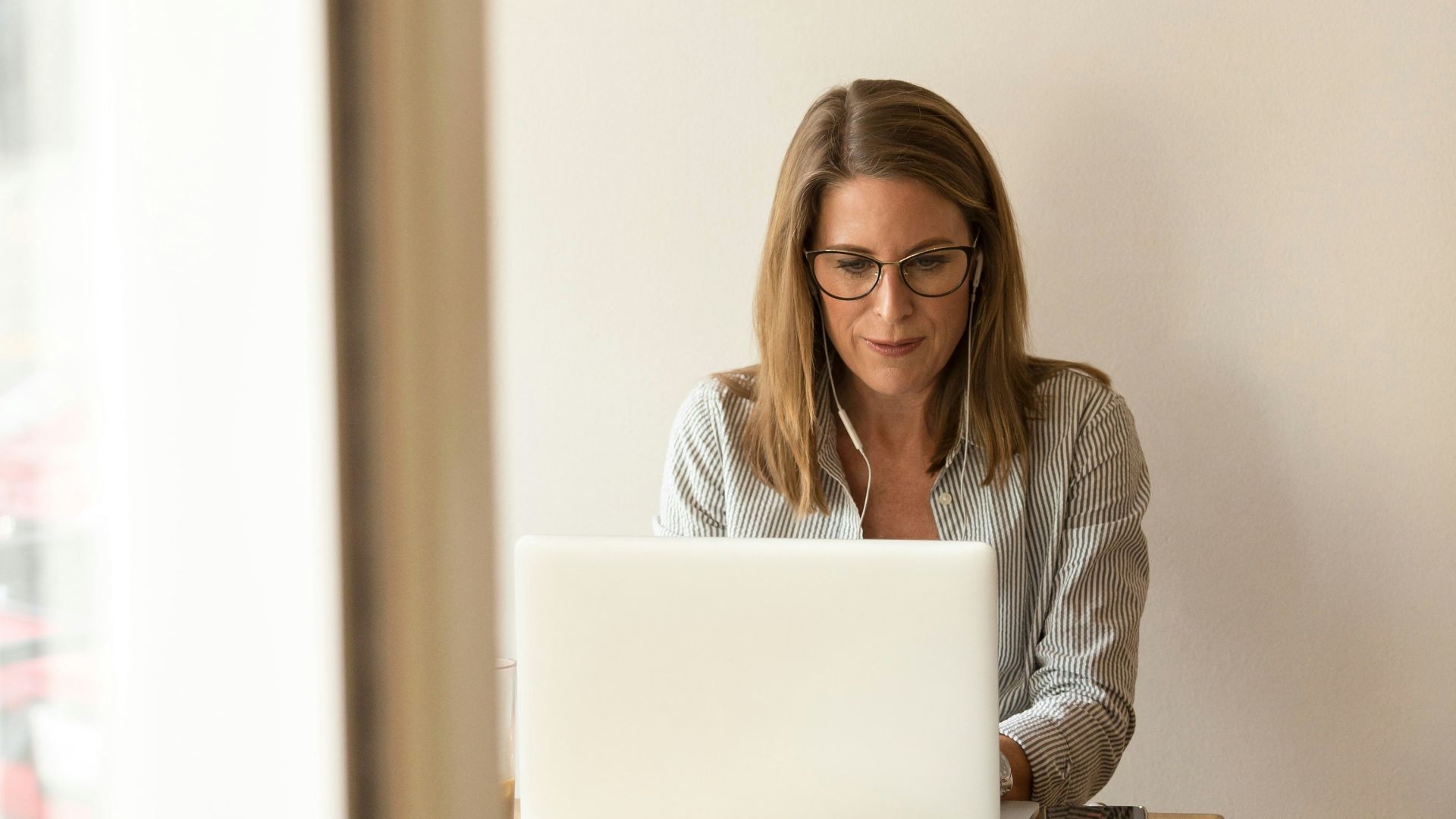 woman wearing grey striped dress shirt sitting down near brown wooden table in front of white laptop computer