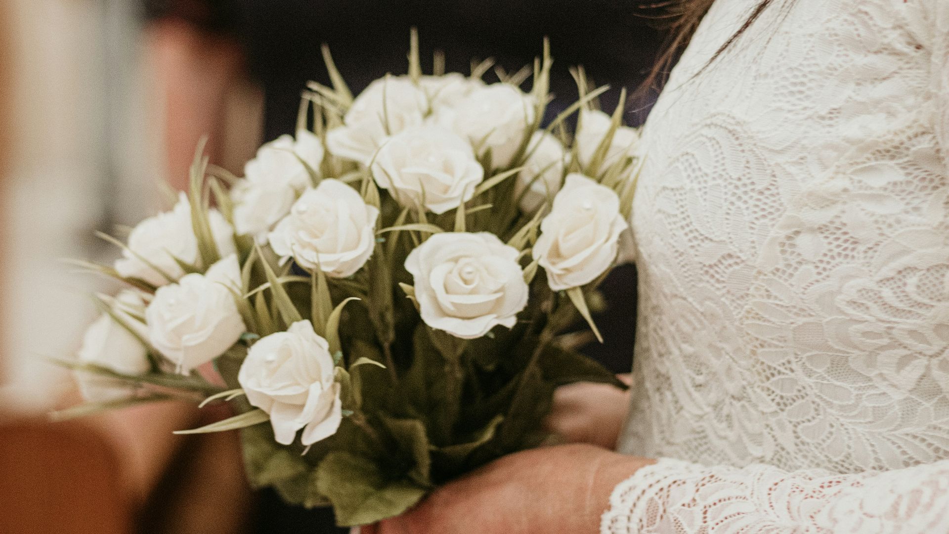 woman in white floral wedding dress holding bouquet of white roses