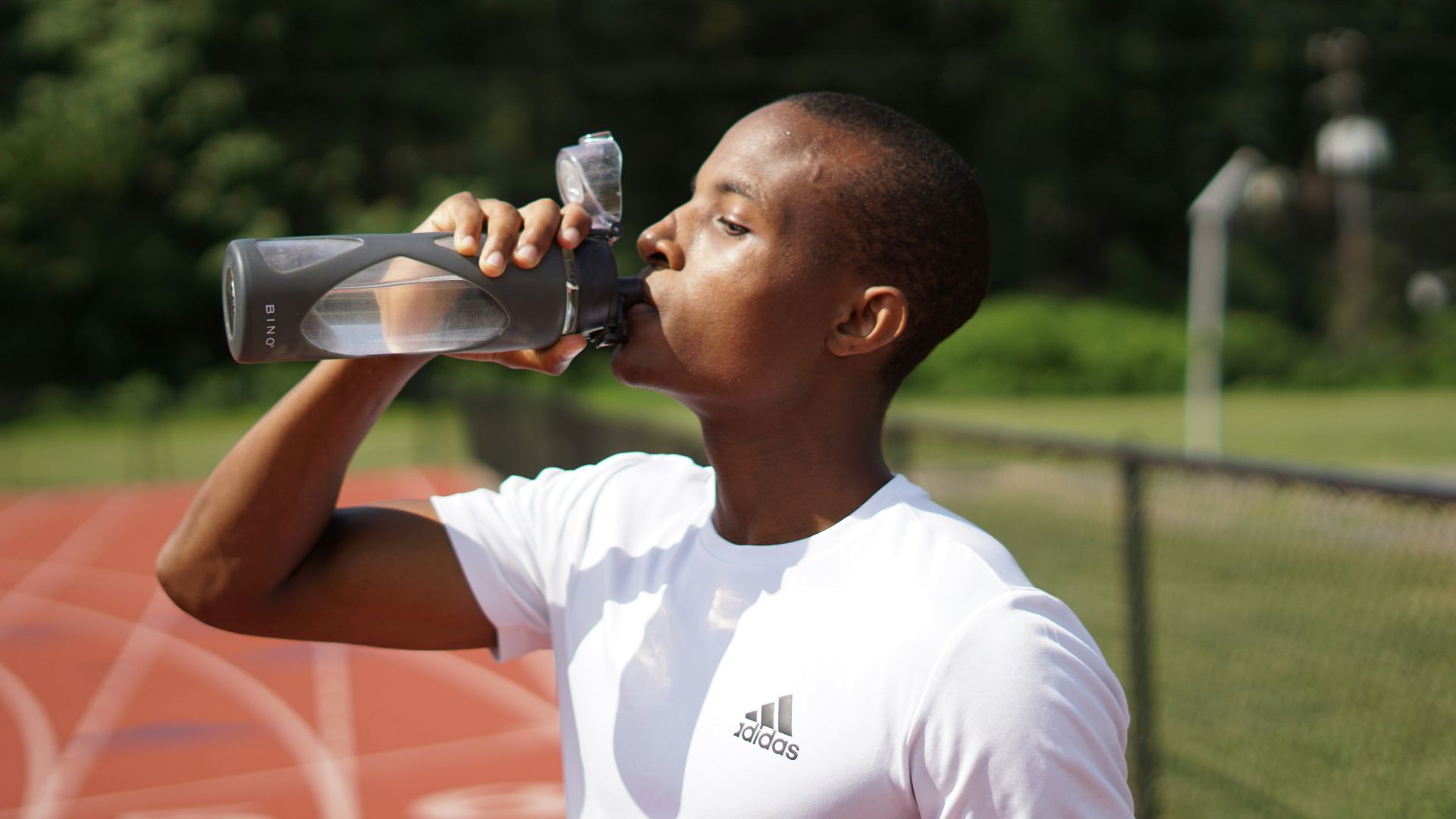 man in white crew neck t-shirt drinking from black sports bottle