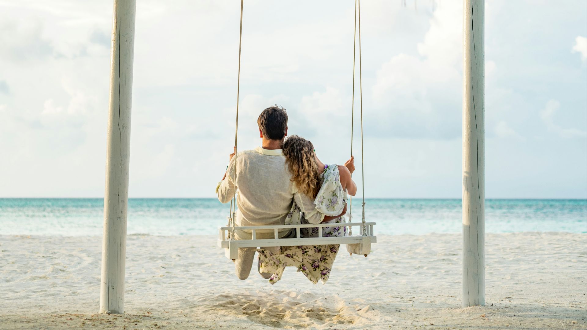 man in white shirt sitting on swing chair under coconut tree during daytime