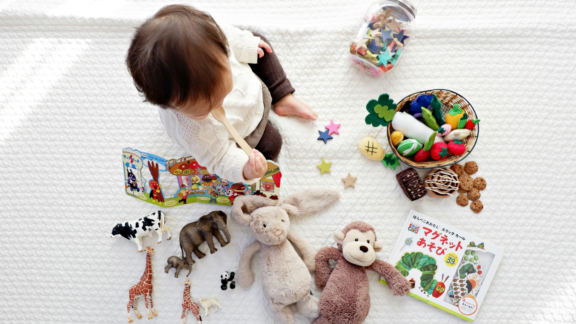 boy sitting on white cloth surrounded by toys