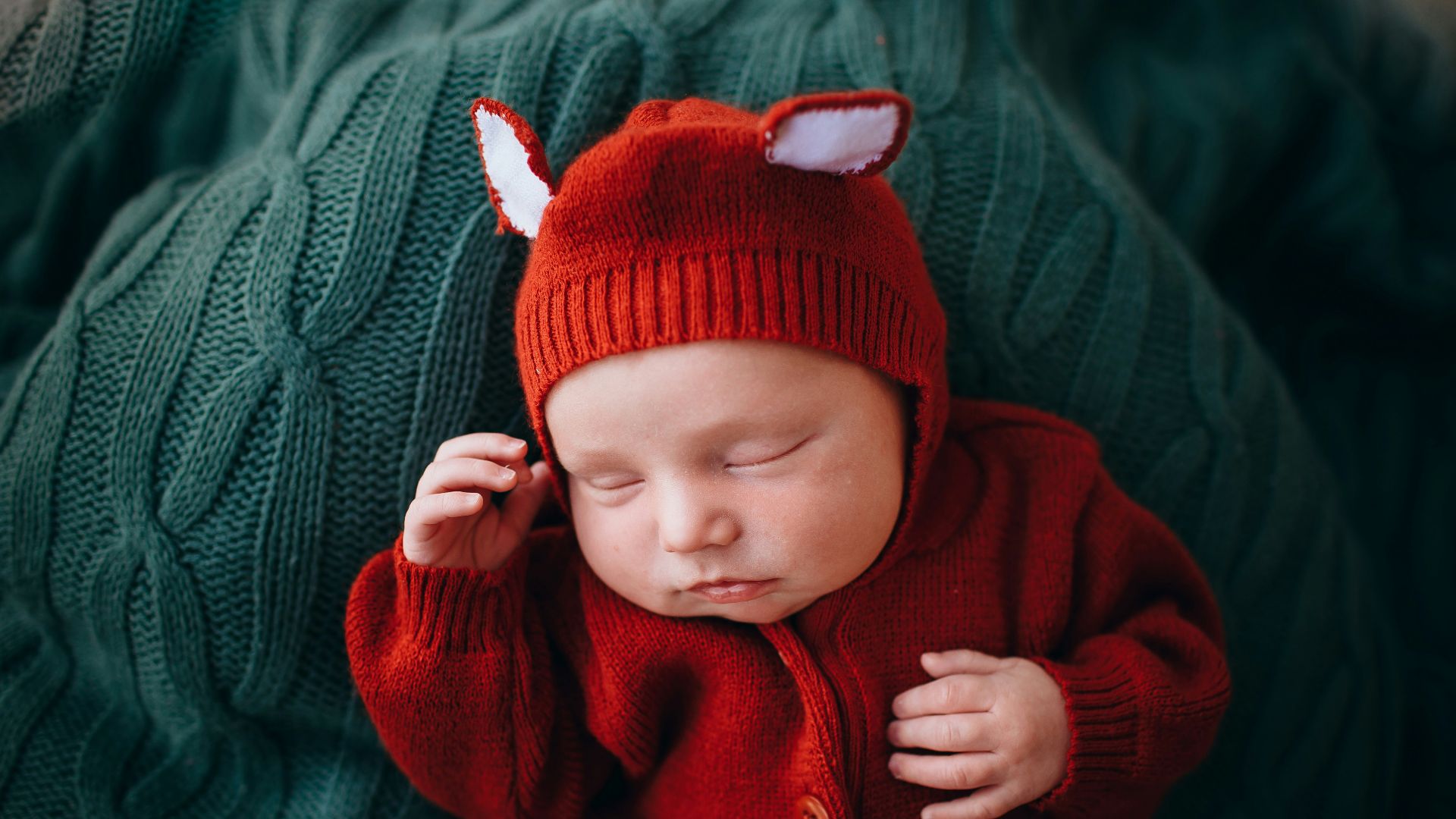baby in red knit cap and red button up jacket
