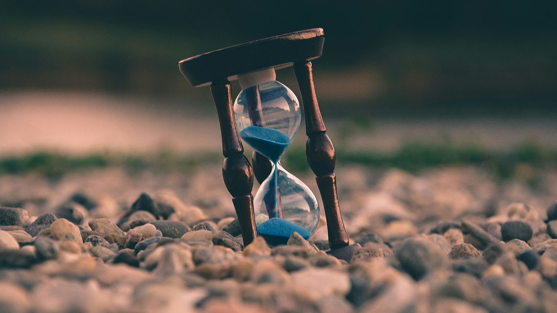 selective focus photo of brown and blue hourglass on stones