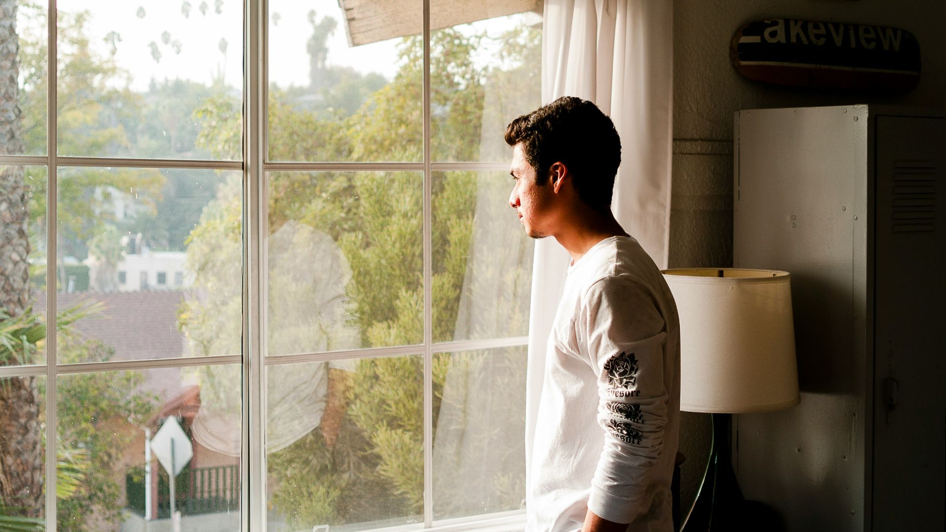 man wearing gray and black crew-neck shirt standing and looking out window