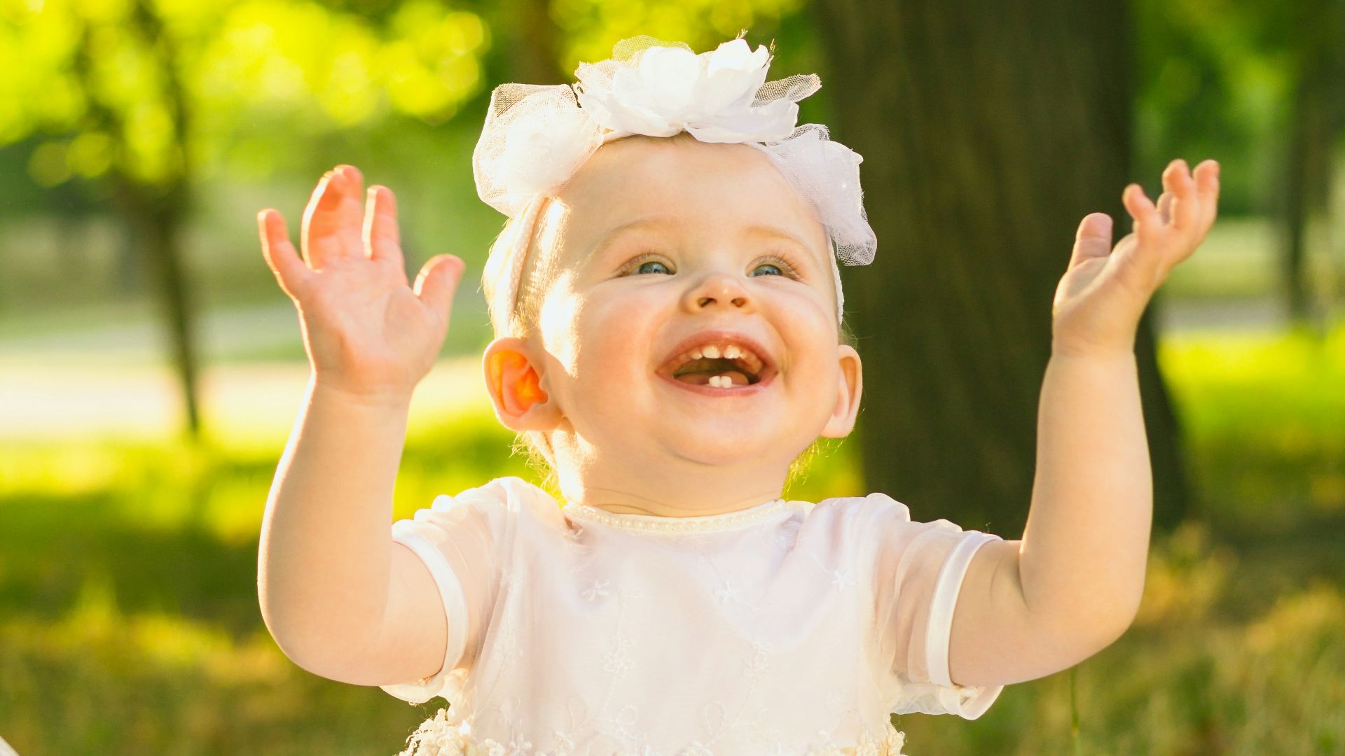 a baby girl in a white dress sitting in the grass
