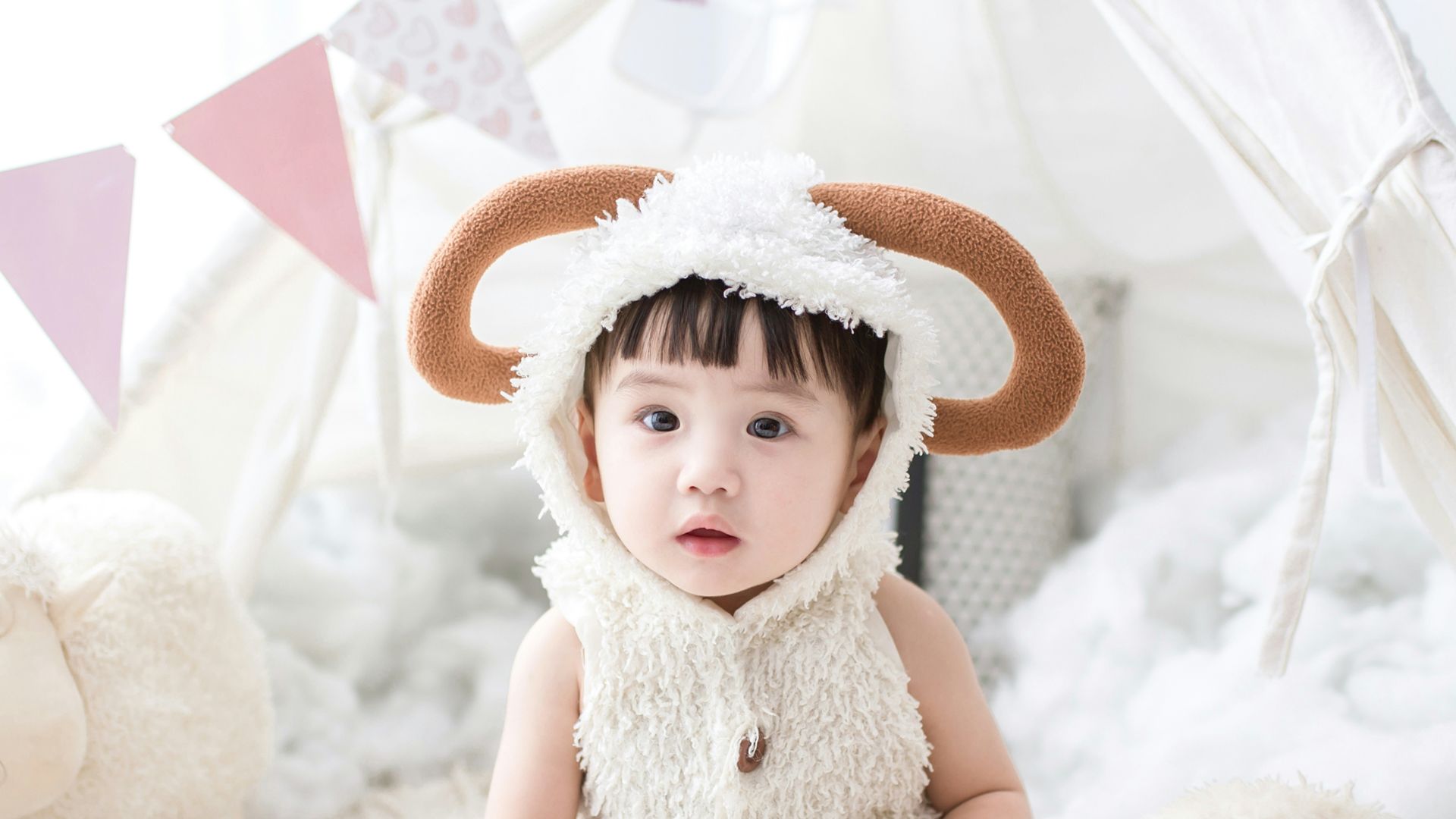 baby sitting beside white sheep plush toy