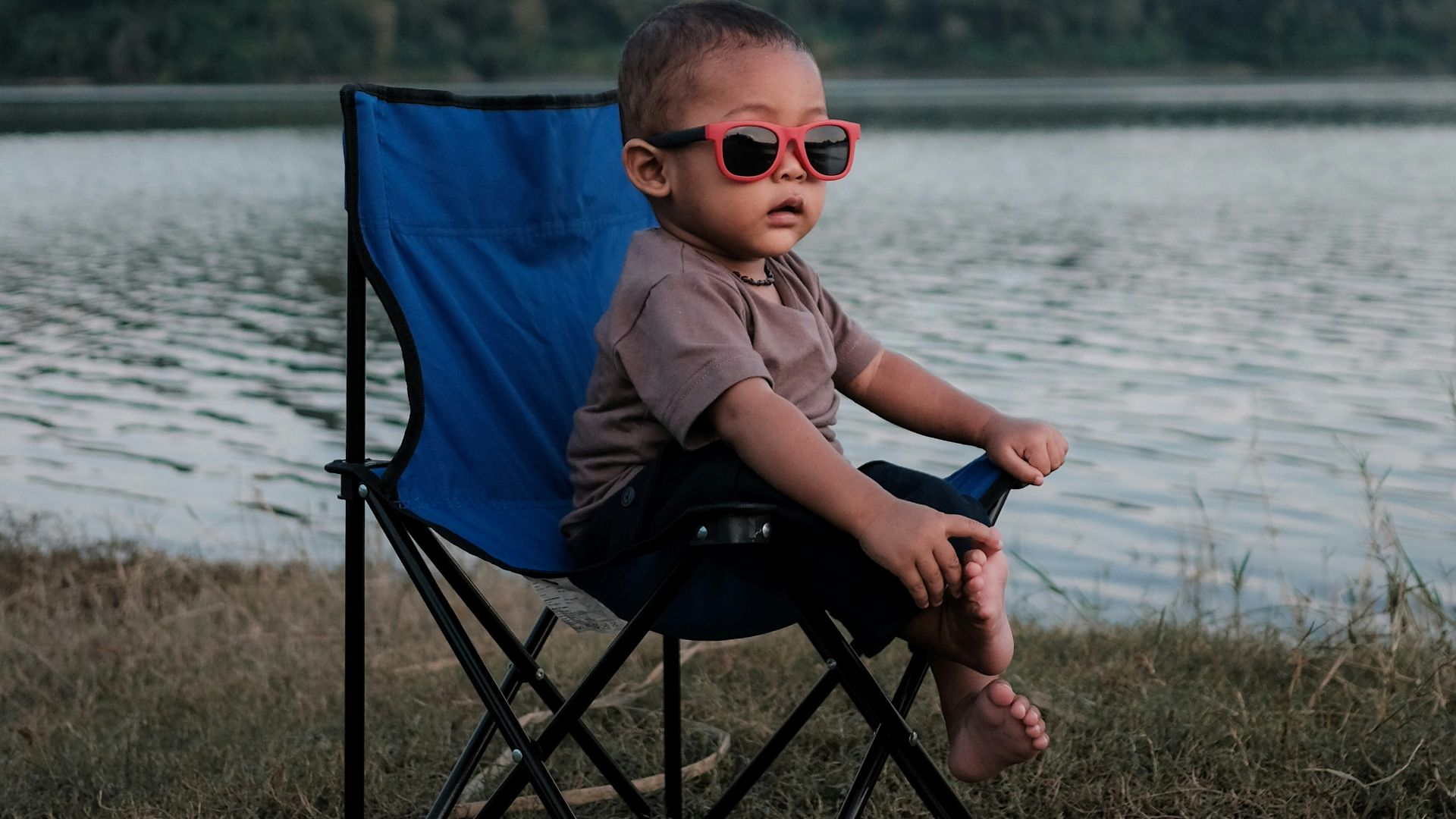boy in gray shirt sitting on blue camping chair near body of water