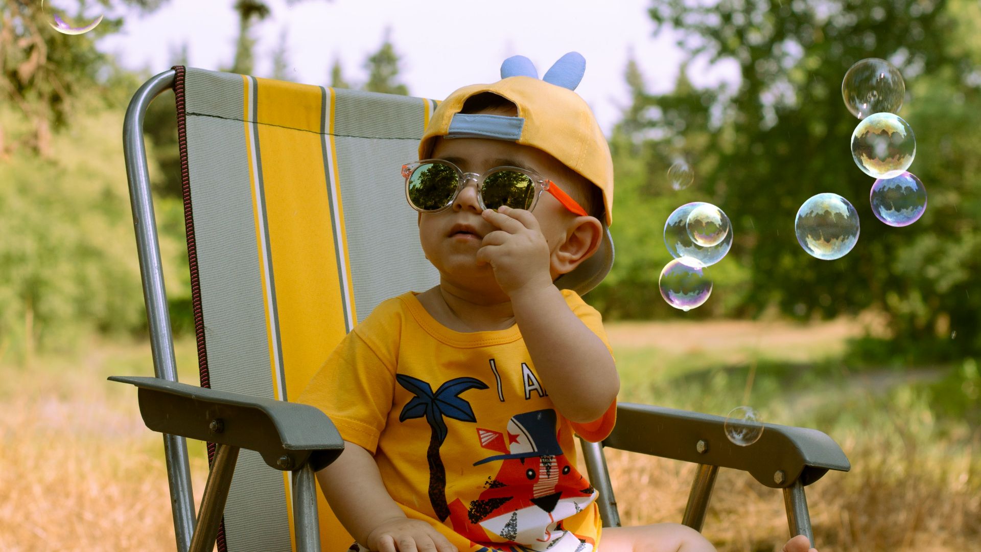 a little boy sitting in a lawn chair blowing bubbles