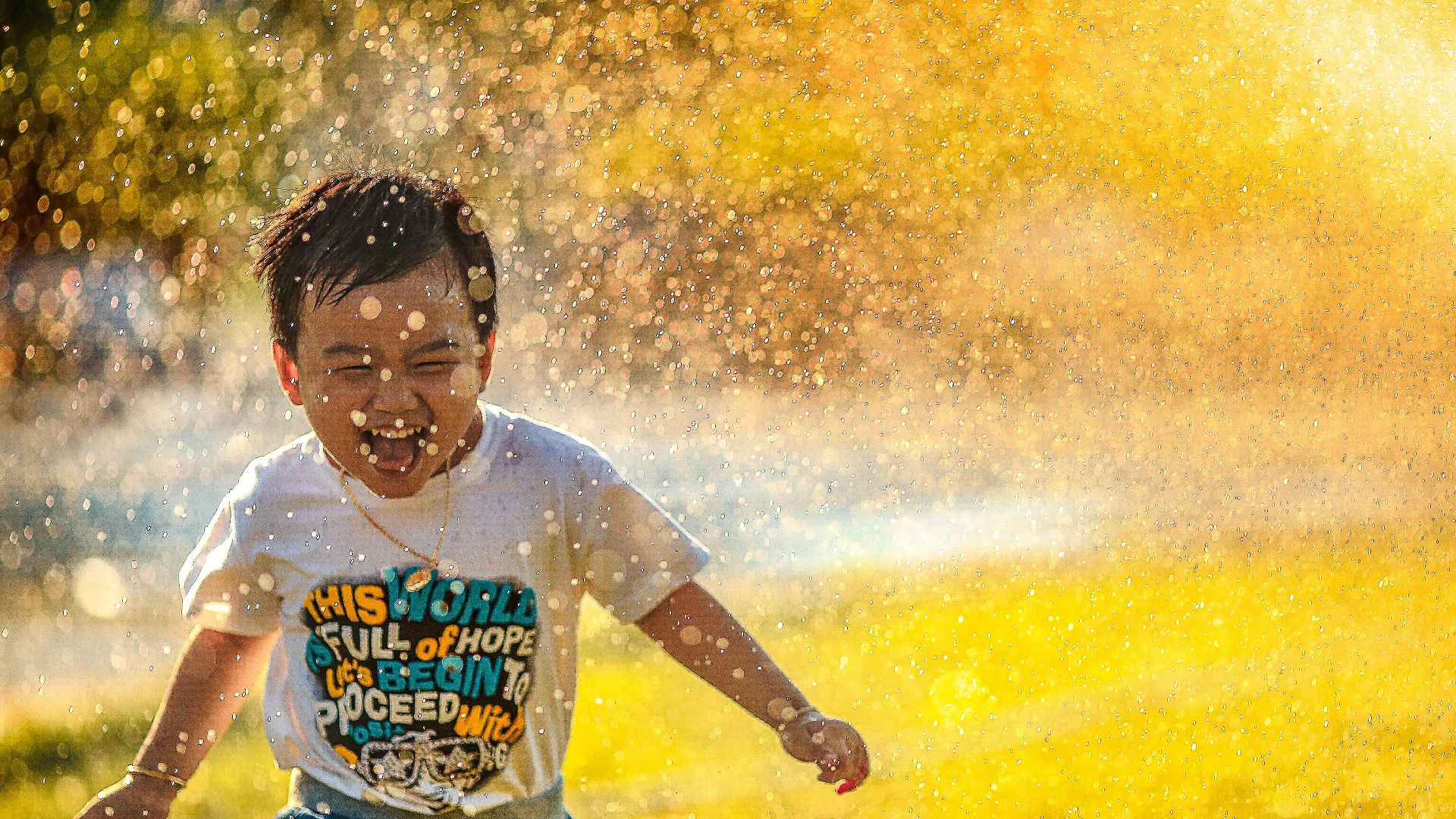 a young boy running through a sprinkle of water