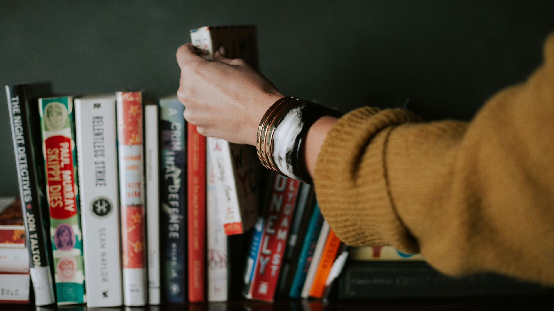 person picking white and red book on bookshelf