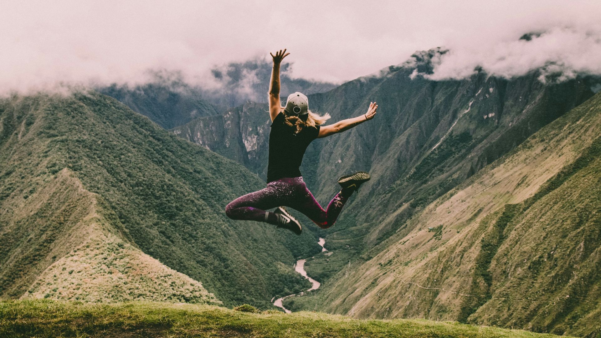 woman jumping on green mountains
