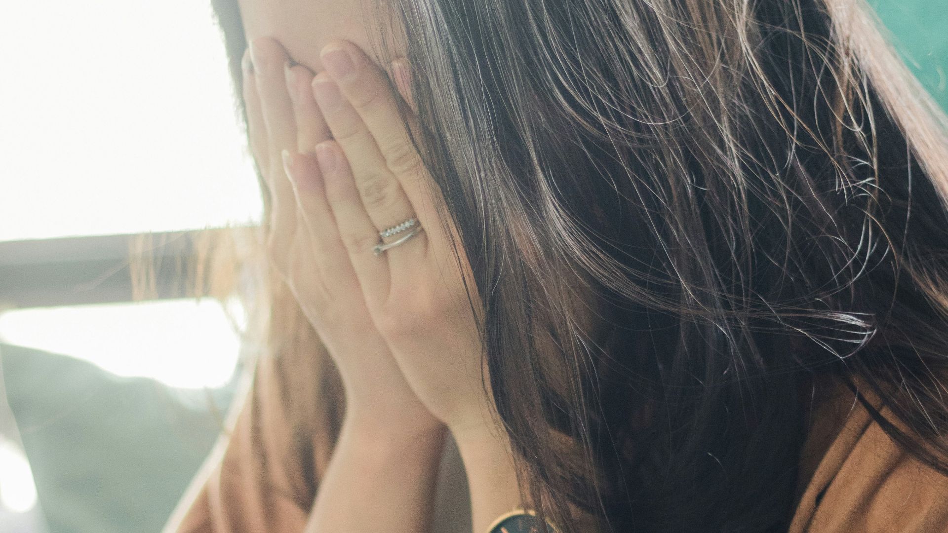woman in brown shirt covering her face