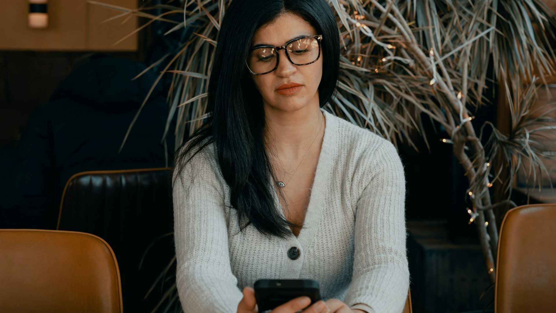 woman in white cardigan holding black smartphone