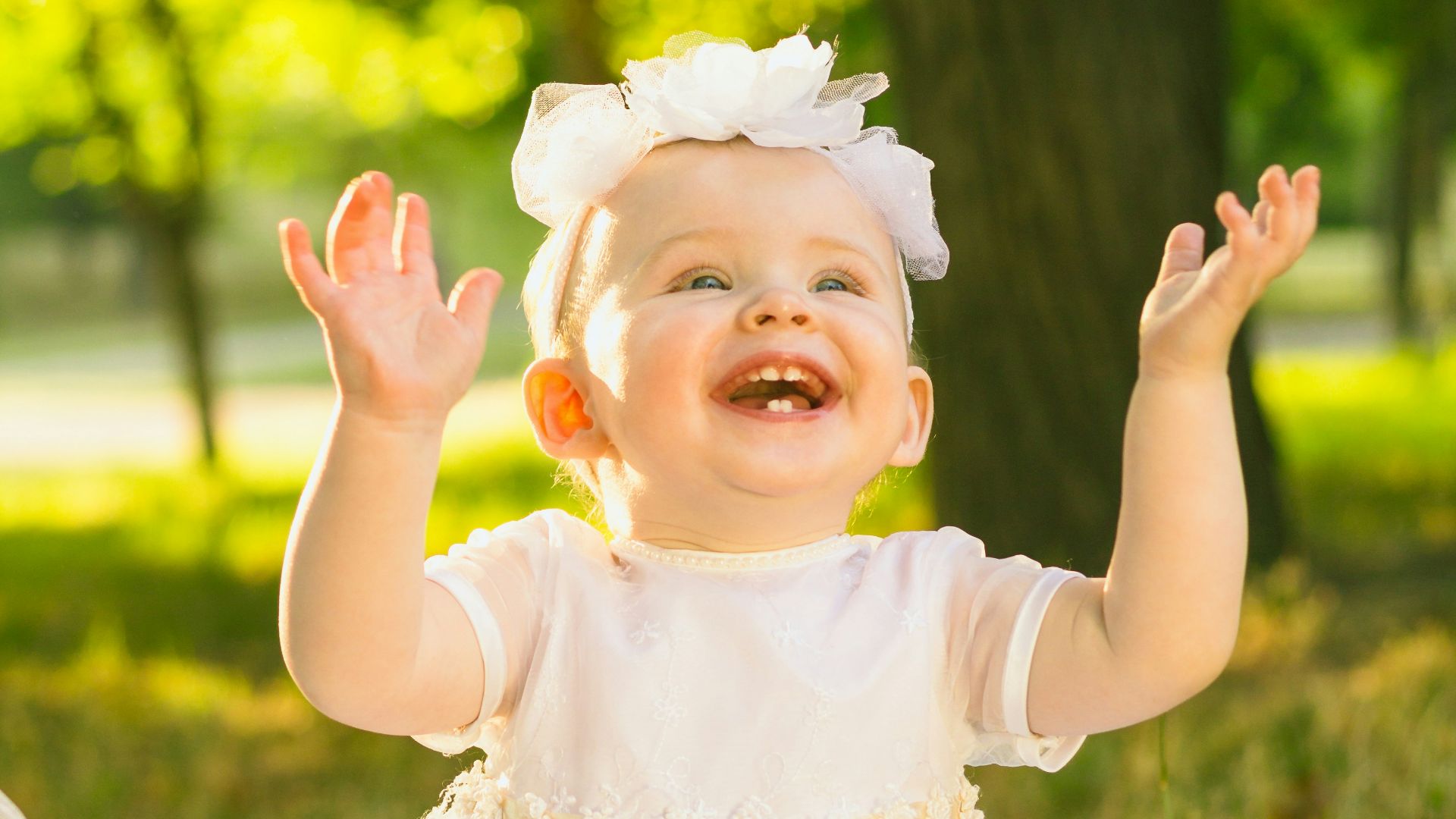 a baby girl in a white dress sitting in the grass