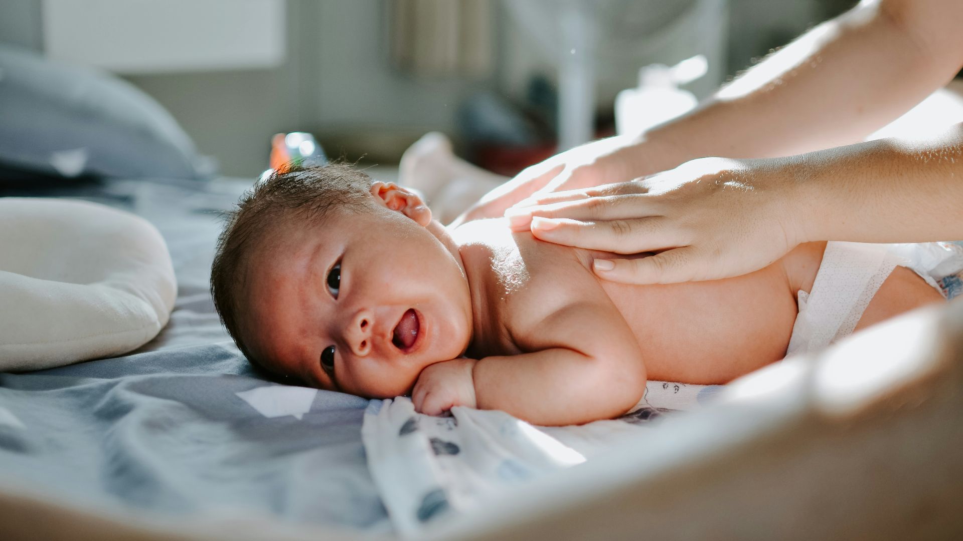 baby laying on bed while woman massaging his back
