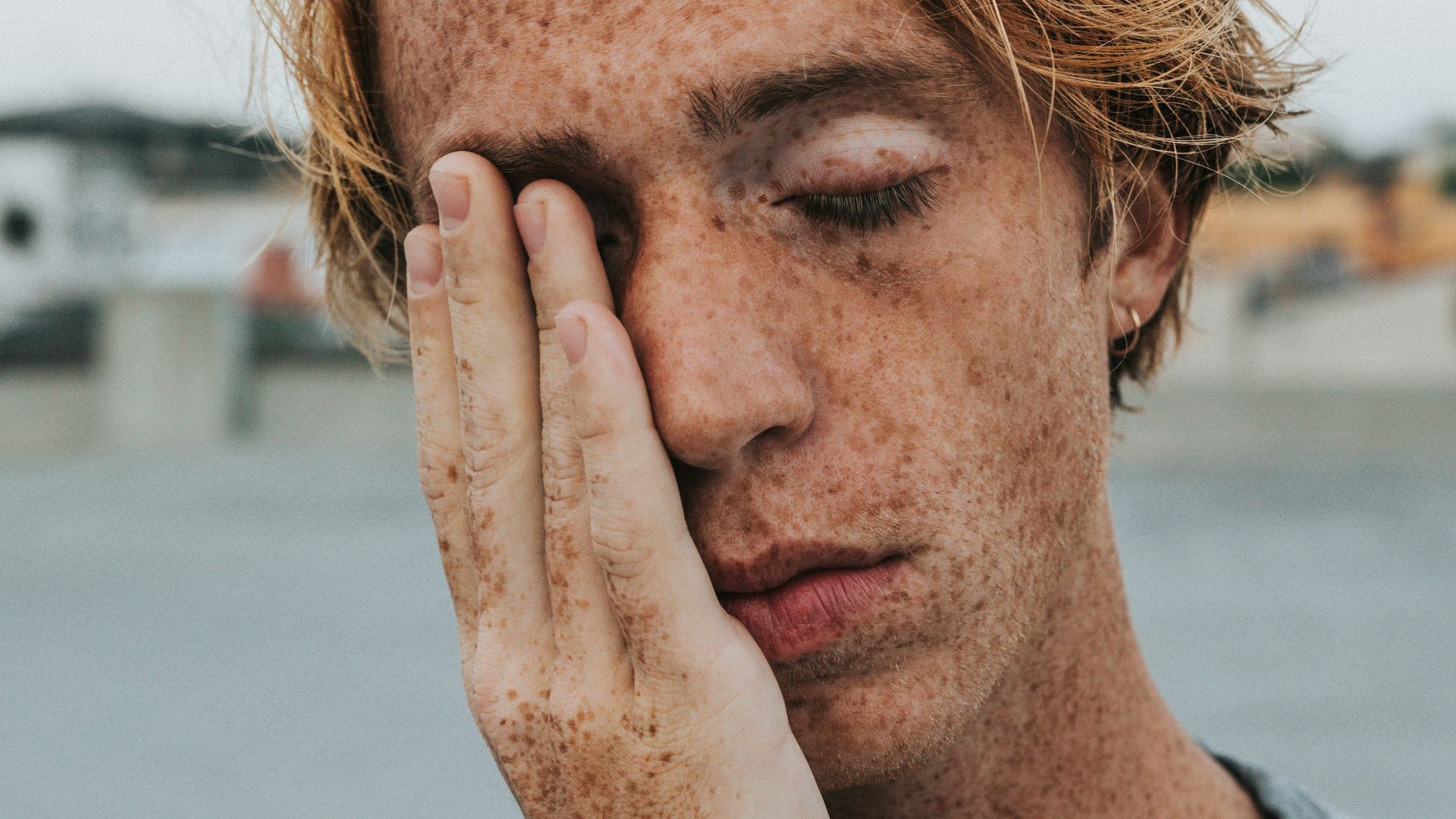 man in gray crew neck shirt covering his face with his hand