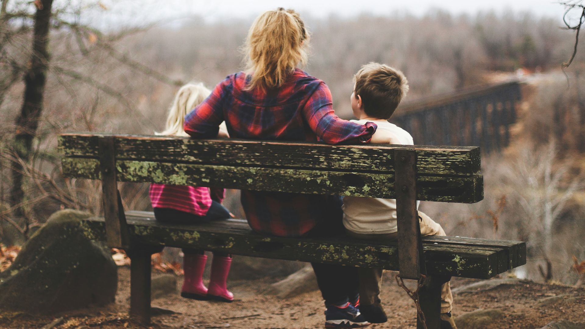 woman between two childrens sitting on brown wooden bench during daytime