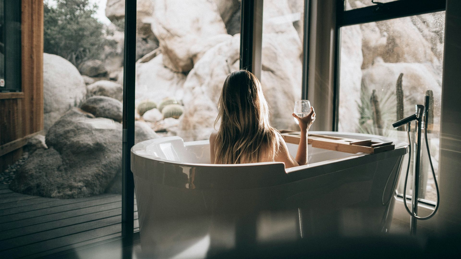 woman in white bathtub holding clear drinking glass