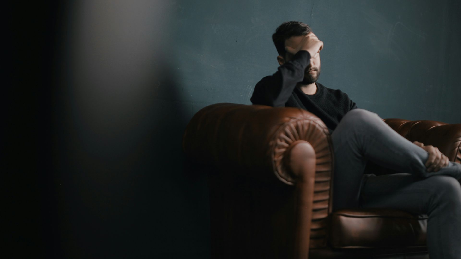 a man holds his head while sitting on a sofa