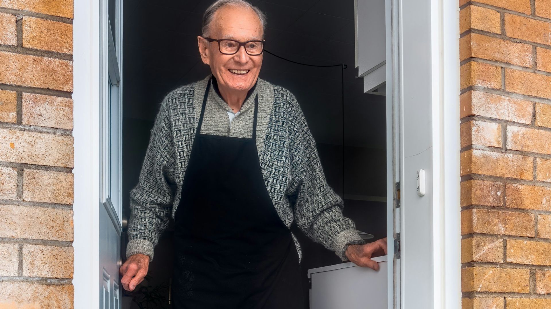 man in black vest and black dress pants standing beside white wooden door