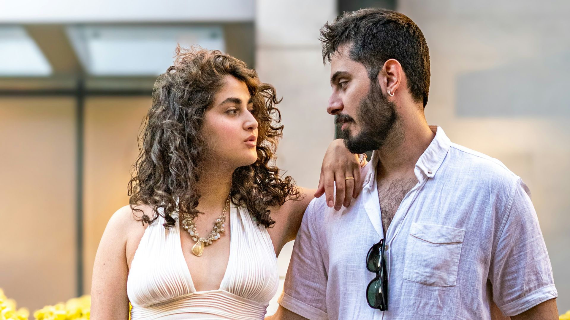 A couple poses together outdoors, looking at each other.