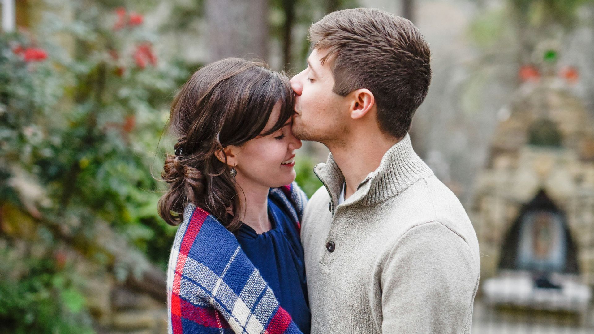 man kissing on woman forehead standing near tree during daytime