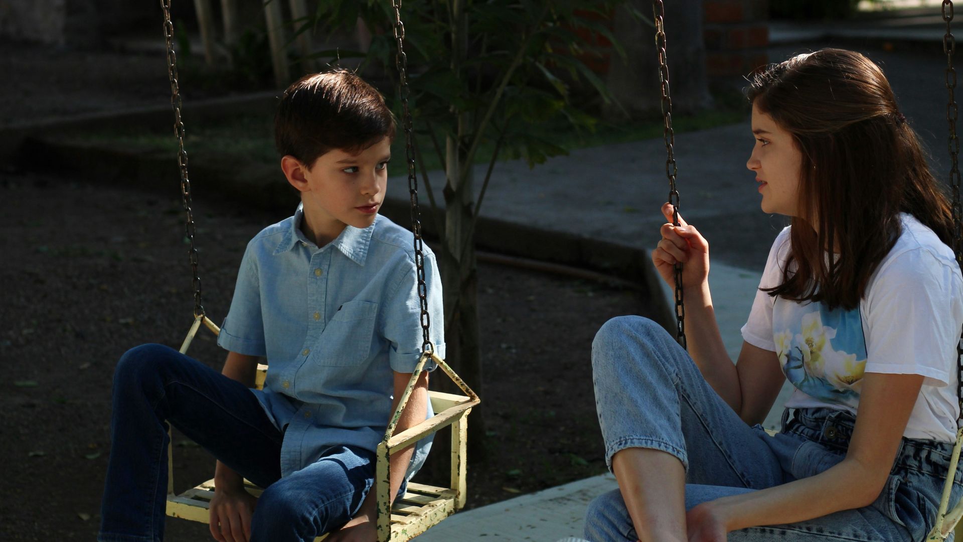boy in blue long sleeve shirt sitting on swing during daytime
