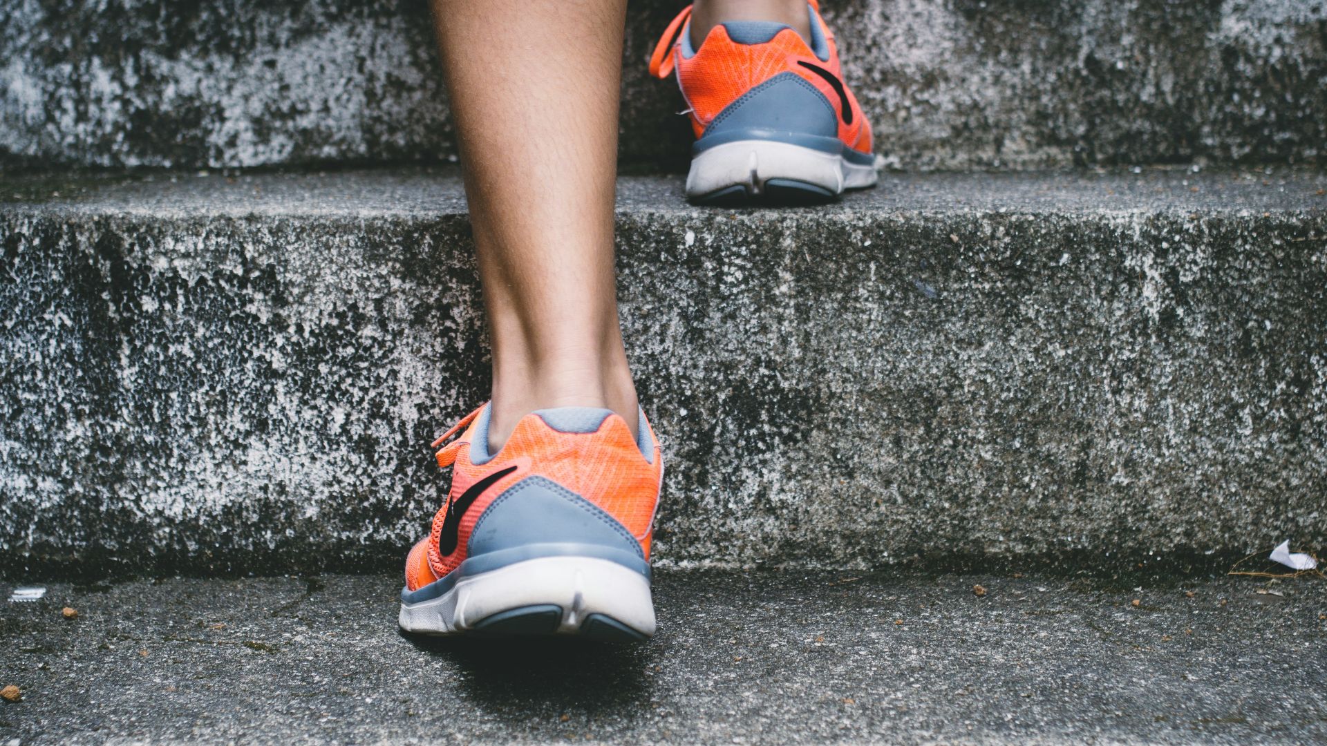 person wearing orange and gray Nike shoes walking on gray concrete stairs