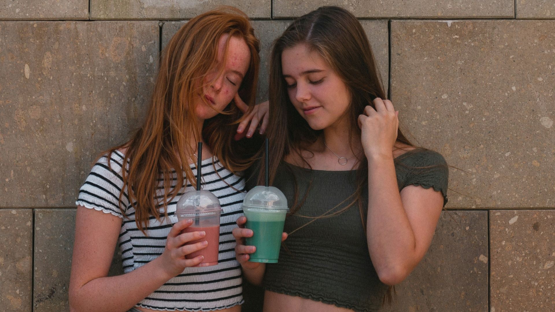 two women leaning on gray wall