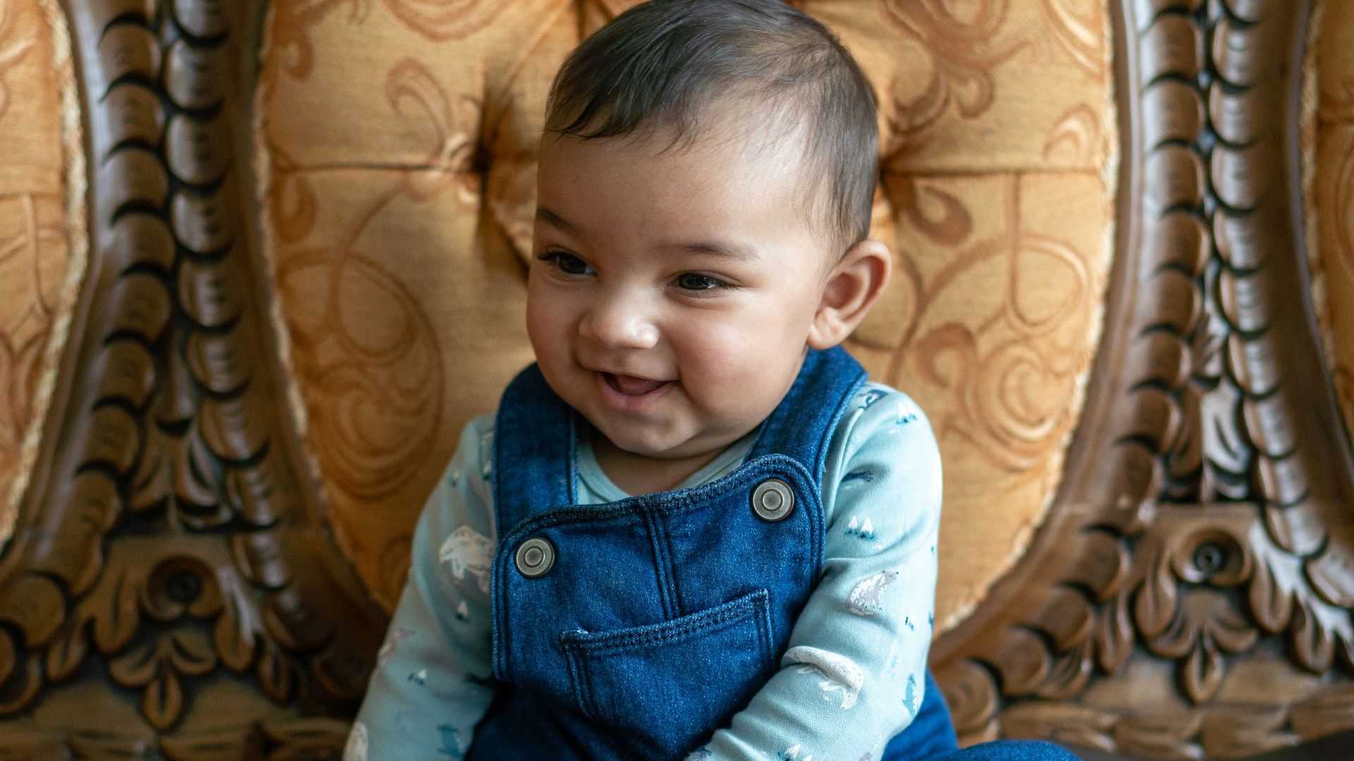 A happy baby smiles while sitting on a couch.
