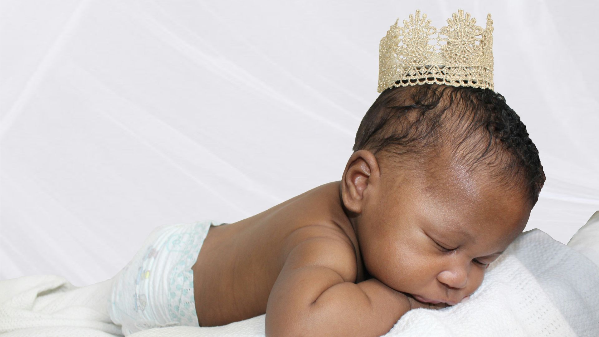 A baby wearing a crown is sleeping on a blanket