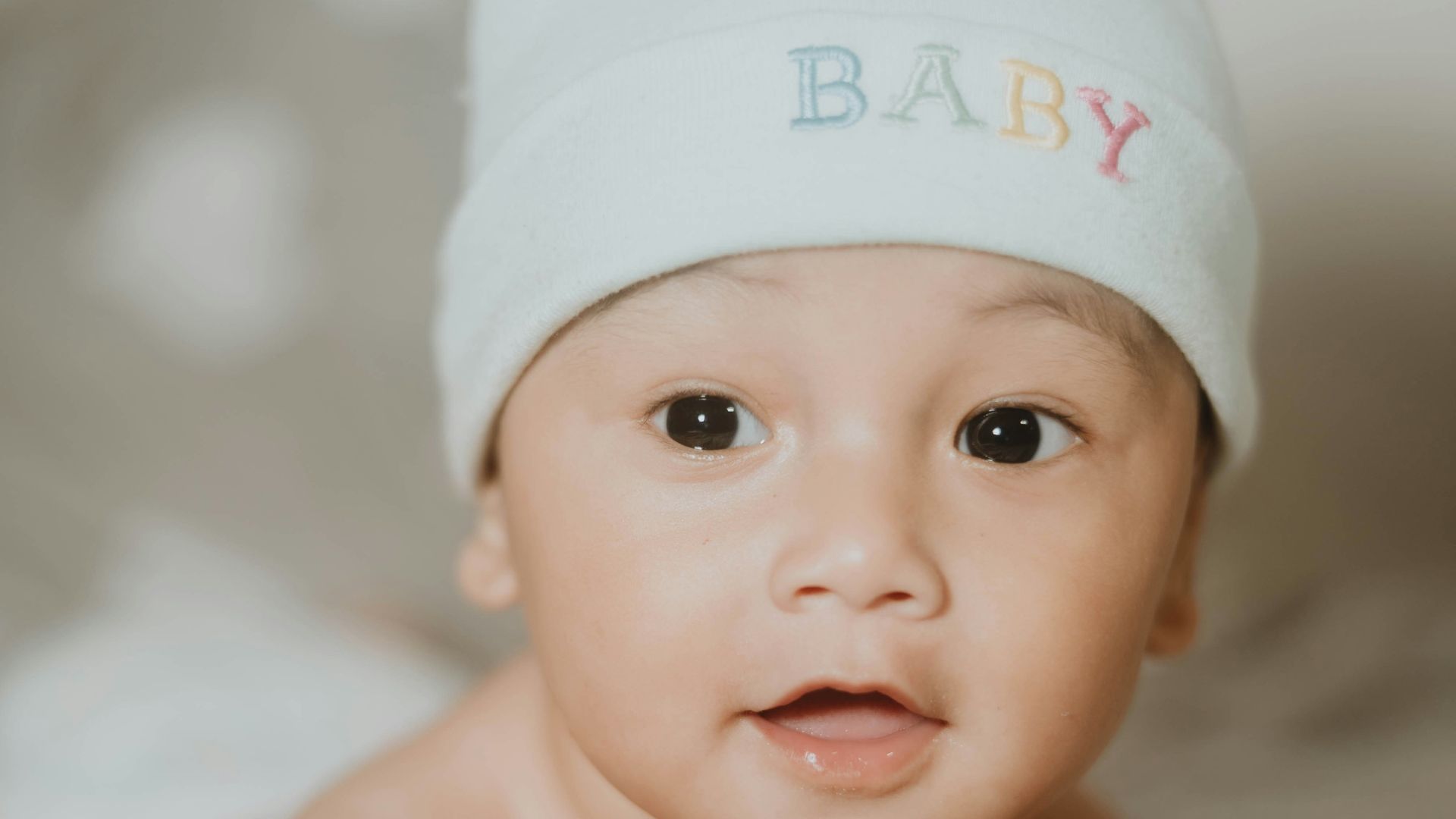 a baby laying on a bed wearing a white hat