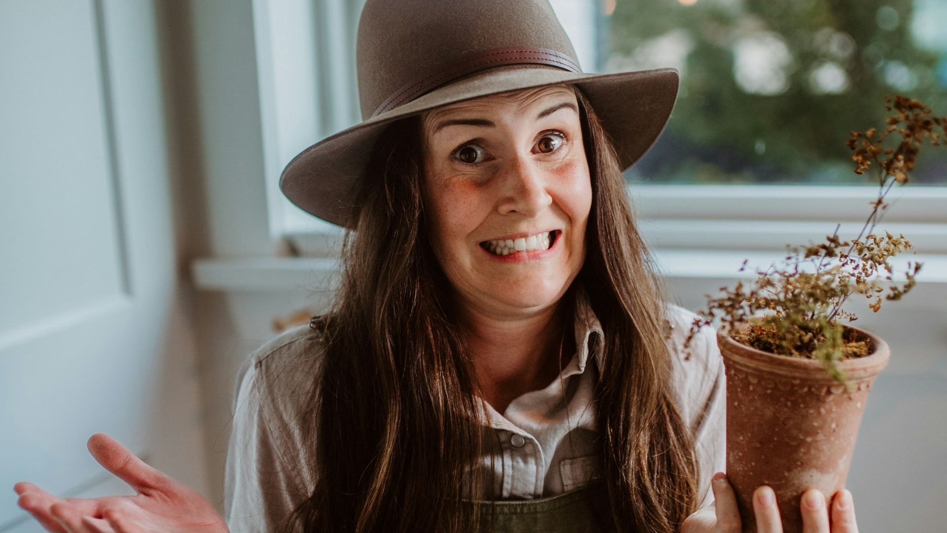 A woman wearing overalls and a hat holding a potted plant