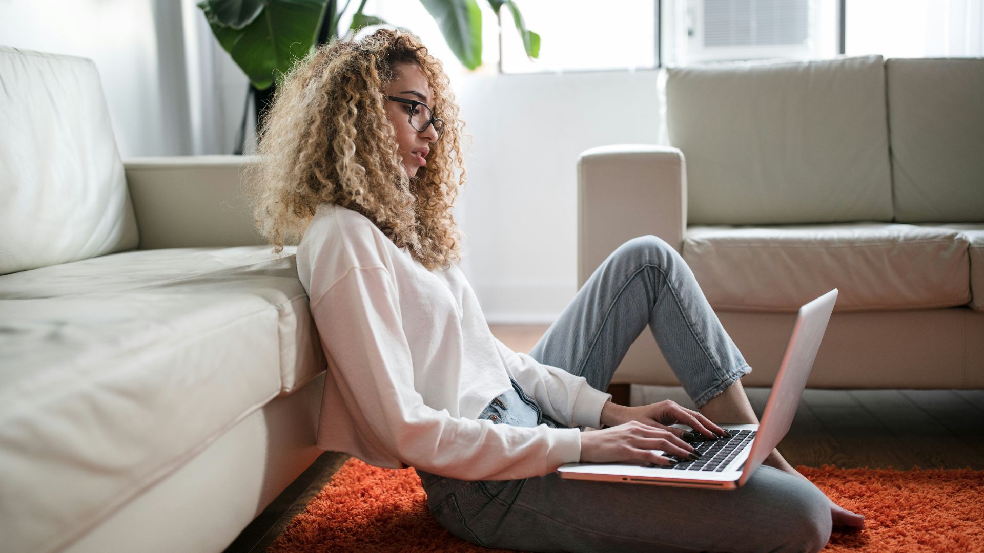 woman sitting on floor and leaning on couch using laptop